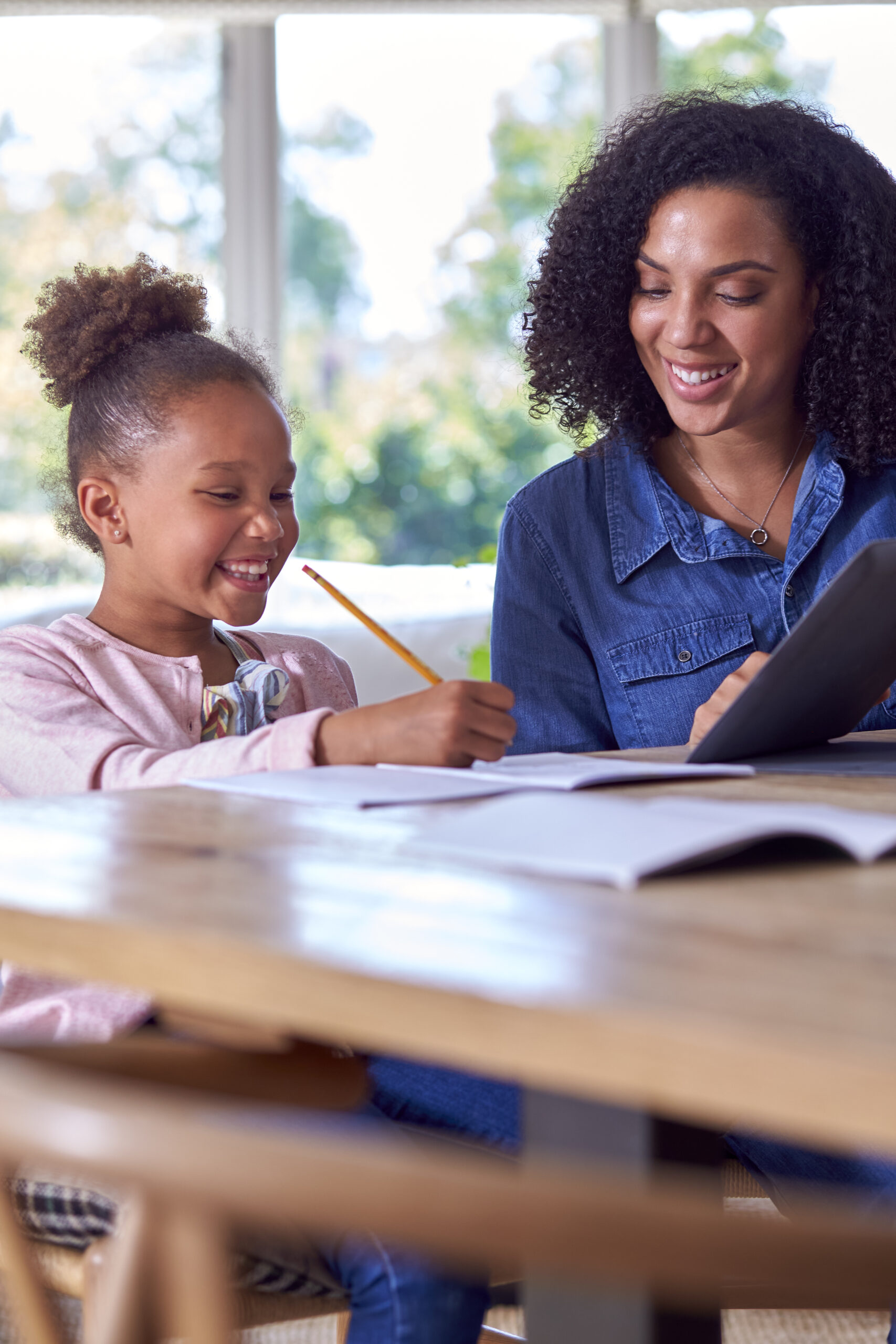 Mother Helping Daughter With Home Schooling Sitting At Table With Digital Tablet
